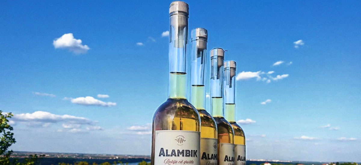 Four bottles of Alambik brandy lined up on a bench represent the Stabarka winery, where Oktopaz designs and manages the construction project - banner