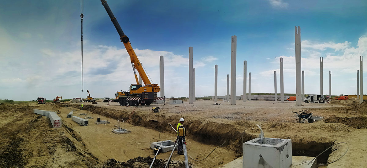 Construction workers, a truck crane, mounted columns and foundations on the CTP Kac industrial facility construction site, where Oktopaz renders construction supervision - banner