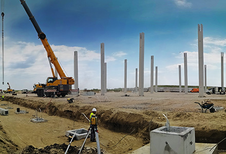Građevinski radnici, autodizalica, montirani stubovi i temelji na gradilištu industrijskog objekta CTP Kać, gde Oktopaz vodi stručni građevinski nadzor - sličica